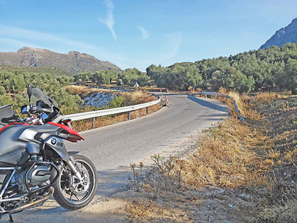 Moto BMW arrêtée au bord d'une route ensoleillée bordée de champs d'oliviers en Andalousie