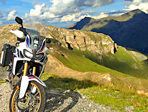 Moto devant un panorama sur les sommets alpins