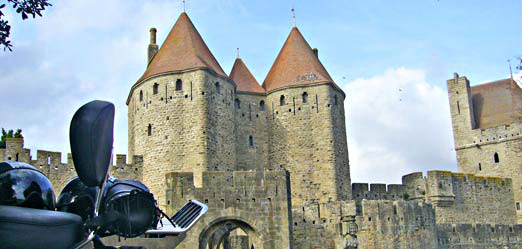 Moto garée devant les murailles et les tours de la Cité de Carcassonne