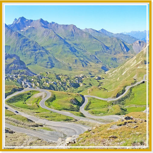 Illustration du voyage moto Alpes : route en lacets au coeur d'une valléé des Alpes en été